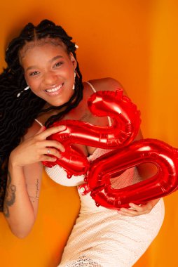 Beyaz elbiseli, turuncu renkli stüdyo zemininde duran genç ve güzel bir doğum günü kızı. Mutlu ve kendinden emin kişi.