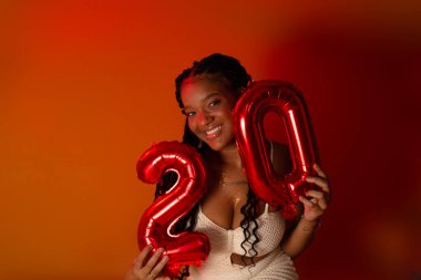 Beyaz elbiseli güzel bir doğum günü kızı turuncu renkli stüdyo zemininde oturuyor. Mutlu ve kendinden emin kişi.