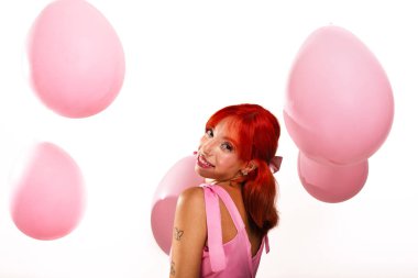 Beyaz arka planda pembe hava balonları arasında kameraya poz veren güzel, kızıl saçlı bir kızın portresi. Stüdyo fotoğrafı
