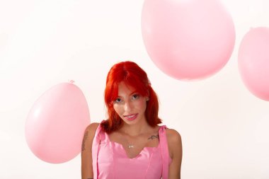 Beyaz arka planda pembe hava balonları arasında kameraya poz veren güzel, kızıl saçlı bir kızın portresi. Stüdyo fotoğrafı