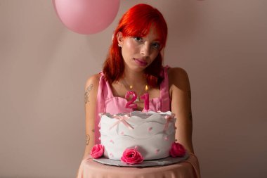 Doğum günü pastasının arkasında açık arkaplanlı pembe elbiseli güzel kızıl saçlı kadın. Stüdyo resmi