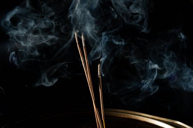 Siyah arka planda duman olan üç yanan tütsü çubuğu. Stüdyo çekimi.
