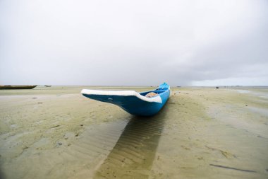 Kuru bir kumsalın kumsalına demirlenmiş mavi balıkçı kanosu. Yoğun bulutlarla dolu çok yağmurlu bir gün. Brezilya