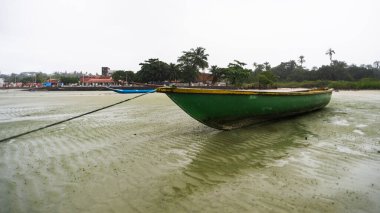 Kuru bir plajın kumsalına demir atmış bir balıkçı teknesi. Yoğun bulutlarla dolu oldukça yağmurlu bir gün. Taşıma araçları.