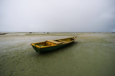 Kuru bir plajın kumsalına demir atmış bir balıkçı teknesi. Yoğun bulutlarla dolu oldukça yağmurlu bir gün. Taşıma araçları.
