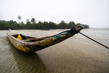 Kuru bir plajın kumlarına demirlenmiş bir balıkçı kanosu. Dalgalar çekildi. Şiddetli bulutlarla dolu yağmurlu bir gün. Taşıma araçları.