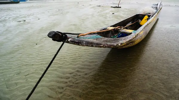 Kuru bir plajın kumlarına demirlenmiş bir balıkçı kanosu. Dalgalar çekildi. Şiddetli bulutlarla dolu yağmurlu bir gün. Taşıma araçları.