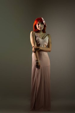 Genç, güzel, kızıl saçlı kız arka planda fotoğraf için poz veriyor. Stüdyo resmi.