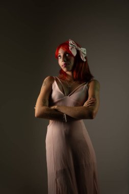 Kolları çapraz duran, koyu arkaplanda fotoğraf çektirmek için poz veren güzel, kızıl saçlı bir kız. Stüdyo resmi