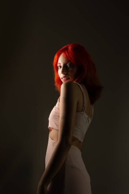 Genç, güzel, kızıl saçlı kız arka planda fotoğraf için poz veriyor. Stüdyo resmi.