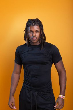 Şort giyen yakışıklı bir adam ve turuncu arka planda fotoğraf için poz veren siyah gömlekli. Kendine güvenen ve sakin biri..