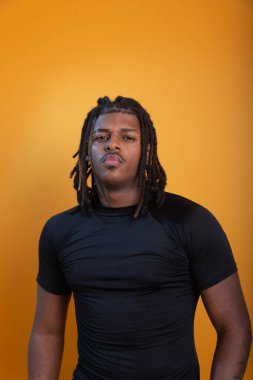 Şort giyen yakışıklı bir adam ve turuncu arka planda fotoğraf için poz veren siyah gömlekli. Kendine güvenen ve sakin biri..