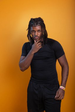 Şort giyen yakışıklı bir adam ve turuncu arka planda fotoğraf için poz veren siyah gömlekli. Kendine güvenen ve sakin biri..