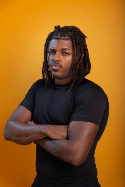 Siyah elbiseli yakışıklı bir gencin stüdyo portresi ve portakal renkli arka planda poz vermesi. Kendine güvenen ve sakin biri..