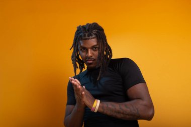 Siyah elbiseli yakışıklı bir gencin stüdyo portresi ve portakal renkli arka planda poz vermesi. Kendine güvenen ve sakin biri..