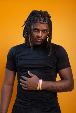 Şort giyen yakışıklı bir adam ve turuncu arka planda fotoğraf için poz veren siyah gömlekli. Kendine güvenen ve sakin biri..