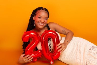 Beyaz elbiseli güzel bir doğum günü kızı turuncu renkli stüdyo zemininde oturuyor. Mutlu ve kendinden emin kişi.