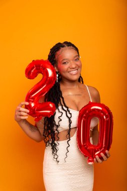 Beyaz elbiseli genç doğum günü kızı turuncu renkli stüdyo zemininde duruyor. Mutlu ve kendinden emin kişi.