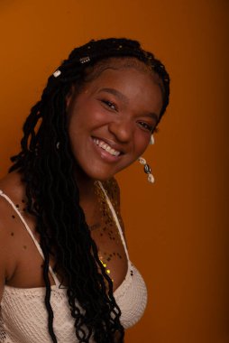 Beyaz elbiseli, mutlu ve parti konfetileri arasında gülümseyen genç bir doğum günü kızı. Koyu turuncu arka planda izole edilmiş. Mutlu ve kendinden emin kişi.