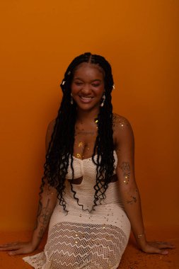 Beyaz elbiseli, mutlu ve gülümseyen genç bir doğum günü kızı koyu turuncu arka planda otururken fotoğraf için poz veriyor. Mutlu ve kendinden emin kişi.