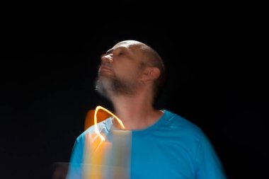 Mavi gömlekli kel adamın sanatsal portresi yanan sarı mumla hareket bulanıklığı yaratıyor. Hafif patika. Siyah arkaplan.