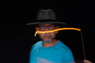 Mavi gömlekli, sakallı kel bir adamın sanatsal portresi. Yanan tütsüyle hafif izler bırakıyor. Hareket bulanıklığı. Siyah arkaplan.