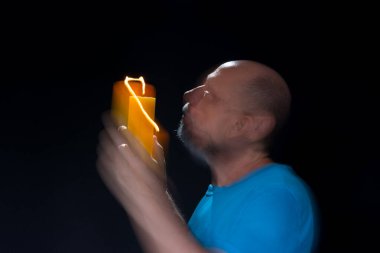 Mavi gömlekli kel adamın sanatsal portresi yanan sarı mumla hareket bulanıklığı yaratıyor. Hafif patika. Siyah arkaplan.