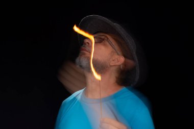 Mavi gömlekli, sakallı kel bir adamın sanatsal portresi. Yanan tütsüyle hafif izler bırakıyor. Hareket bulanıklığı. Siyah arkaplan.