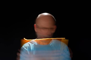 Mavi gömlekli kel adamın sanatsal portresi yanan sarı mumla hareket bulanıklığı yaratıyor. Hafif patika. Siyah arkaplan.