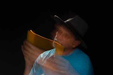 Mavi tişörtlü, sakallı, kel, şapkalı, yanan mumla ışık saçan adamın sanatsal portresi. Hareket bulanıklığı. Siyah arkaplan.