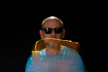 Mavi gömlekli kel adamın sanatsal portresi yanan sarı mumla hareket bulanıklığı yaratıyor. Hafif patika. Siyah arkaplan.