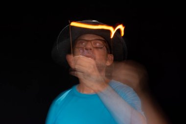 Mavi gömlekli, sakallı kel bir adamın sanatsal portresi. Yanan tütsüyle hafif izler bırakıyor. Hareket bulanıklığı. Siyah arkaplan.