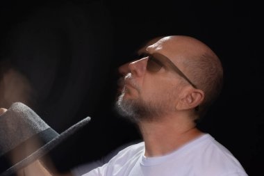 Beyaz gömlekli sakallı kel adamın sanatsal portresi elleri ve kollarıyla hareket bulanıklığı yaratıyor. Siyah arkaplan.