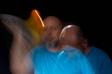 Mavi gömlekli kel adamın sanatsal portresi yanan sarı mumla hareket bulanıklığı yaratıyor. Hafif patika. Siyah arkaplan.