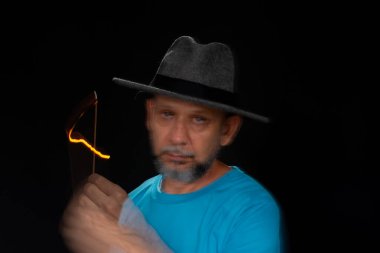 Mavi gömlekli, sakallı kel bir adamın sanatsal portresi. Yanan tütsüyle hafif izler bırakıyor. Hareket bulanıklığı. Siyah arkaplan.