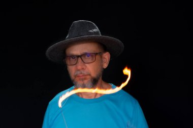 Mavi gömlekli, sakallı kel bir adamın sanatsal portresi. Yanan tütsüyle hafif izler bırakıyor. Hareket bulanıklığı. Siyah arkaplan.