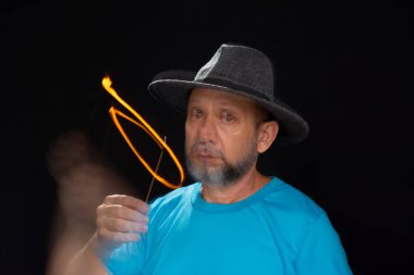 Mavi gömlekli, sakallı kel bir adamın sanatsal portresi. Yanan tütsüyle hafif izler bırakıyor. Hareket bulanıklığı. Siyah arkaplan.