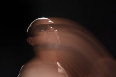 Hareket bulanıklığı efektli güneş gözlüğü takan sakalsız kel adamın sanatsal portresi. Siyah arkaplan.