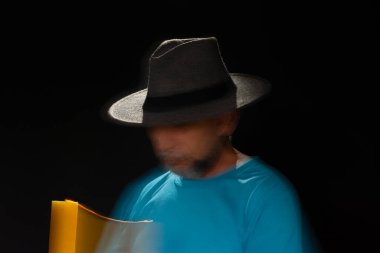 Mavi tişörtlü, sakallı, kel, şapkalı, yanan mumla ışık saçan adamın sanatsal portresi. Hareket bulanıklığı. Siyah arkaplan.