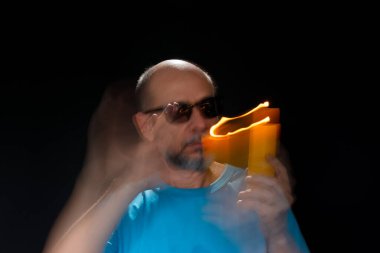 Mavi gömlekli kel adamın sanatsal portresi yanan sarı mumla hareket bulanıklığı yaratıyor. Hafif patika. Siyah arkaplan.