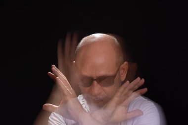 Beyaz gömlekli sakallı kel adamın sanatsal portresi elleri ve kollarıyla hareket bulanıklığı yaratıyor. Siyah arkaplan.