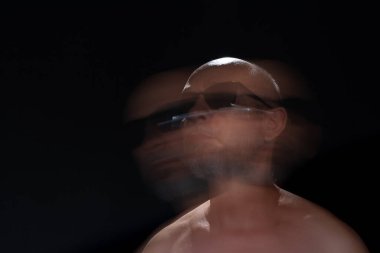 Hareket bulanıklığı efektli güneş gözlüğü takan sakalsız kel adamın sanatsal portresi. Siyah arkaplan.