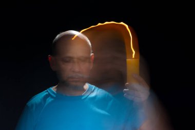 Mavi gömlekli kel adamın sanatsal portresi yanan sarı mumla hareket bulanıklığı yaratıyor. Hafif patika. Siyah arkaplan.