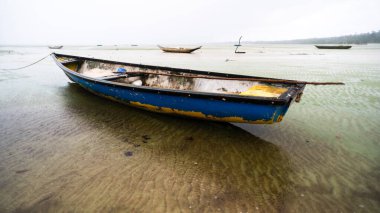 Kuru bir plajın kumsalına demir atmış bir balıkçı teknesi. Yoğun bulutlarla dolu oldukça yağmurlu bir gün. Taşıma araçları.