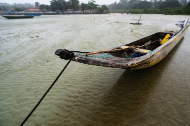 Kuru bir plajın kumlarına demirlenmiş bir balıkçı kanosu. Dalgalar çekildi. Şiddetli bulutlarla dolu yağmurlu bir gün. Taşıma araçları.