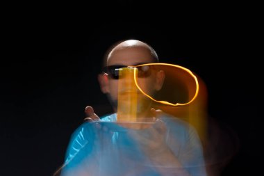 Mavi gömlekli kel adamın sanatsal portresi yanan sarı mumla hareket bulanıklığı yaratıyor. Hafif patika. Siyah arkaplan.