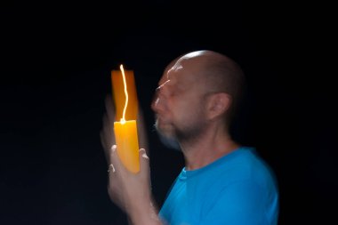 Mavi gömlekli kel adamın sanatsal portresi yanan sarı mumla hareket bulanıklığı yaratıyor. Hafif patika. Siyah arkaplan.