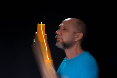 Mavi gömlekli kel adamın sanatsal portresi yanan sarı mumla hareket bulanıklığı yaratıyor. Hafif patika. Siyah arkaplan.