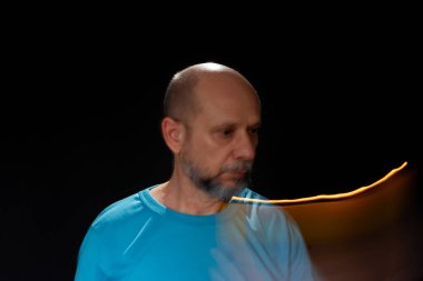 Mavi gömlekli kel adamın sanatsal portresi yanan sarı mumla hareket bulanıklığı yaratıyor. Hafif patika. Siyah arkaplan.