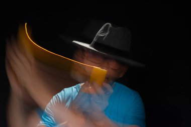 Mavi tişörtlü, sakallı, kel, şapkalı, yanan mumla ışık saçan adamın sanatsal portresi. Hareket bulanıklığı. Siyah arkaplan.